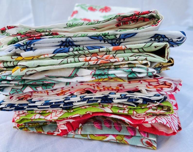 May include: A stack of colorful fabric napkins with floral patterns. The napkins are folded and stacked on top of each other, creating a layered effect. The napkins are made of cotton and have a soft, comfortable feel.