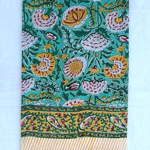 May include: A rectangular fabric with a floral pattern in teal, yellow, red, and green. The design includes large flowers and a border with paisley and striped details. The material is likely cotton or linen, suitable for home decor or crafting purposes.