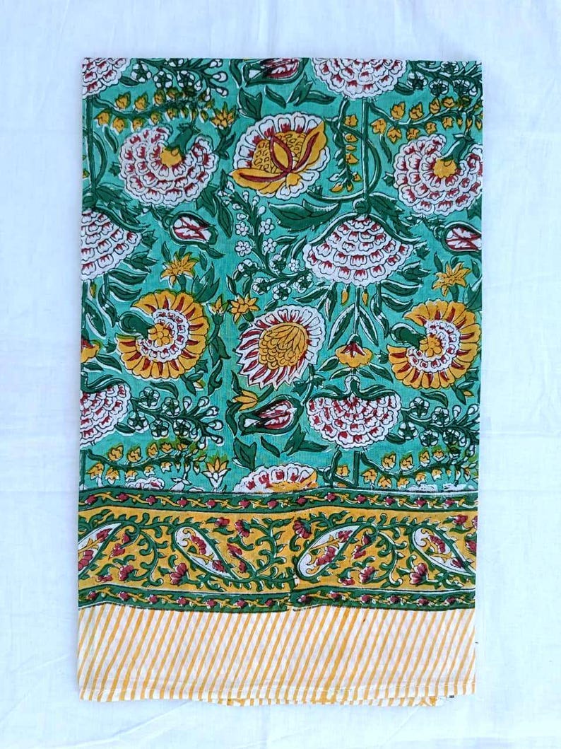 May include: A rectangular fabric with a floral pattern in teal, yellow, red, and green. The design includes large flowers and a border with paisley and striped details. The material is likely cotton or linen, suitable for home decor or crafting purposes.