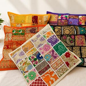 May include: A collection of four square throw pillows featuring intricate patchwork designs. Each pillow is composed of various fabric squares in vibrant colors including orange, purple, black, and cream, decorated with detailed embroidery and patterns.