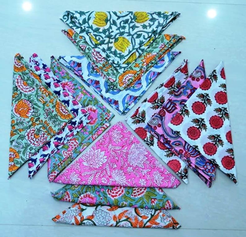 May include: A set of 10 colorful cotton napkins with floral patterns. The napkins are folded into triangles and arranged in a star shape. The napkins are in shades of pink, green, blue, and white.