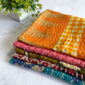 May include: A stack of colorful, stitched fabric pieces. The top piece is orange and yellow with a geometric pattern. Below are pieces in pink, green, red, and blue, each with unique patterns. The fabrics appear to be handmade, possibly quilts or throws.