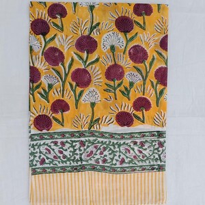 May include: A folded yellow textile with a floral pattern. The design features burgundy and white flowers with green stems and leaves. The bottom border has a green and white paisley design and yellow stripes.
