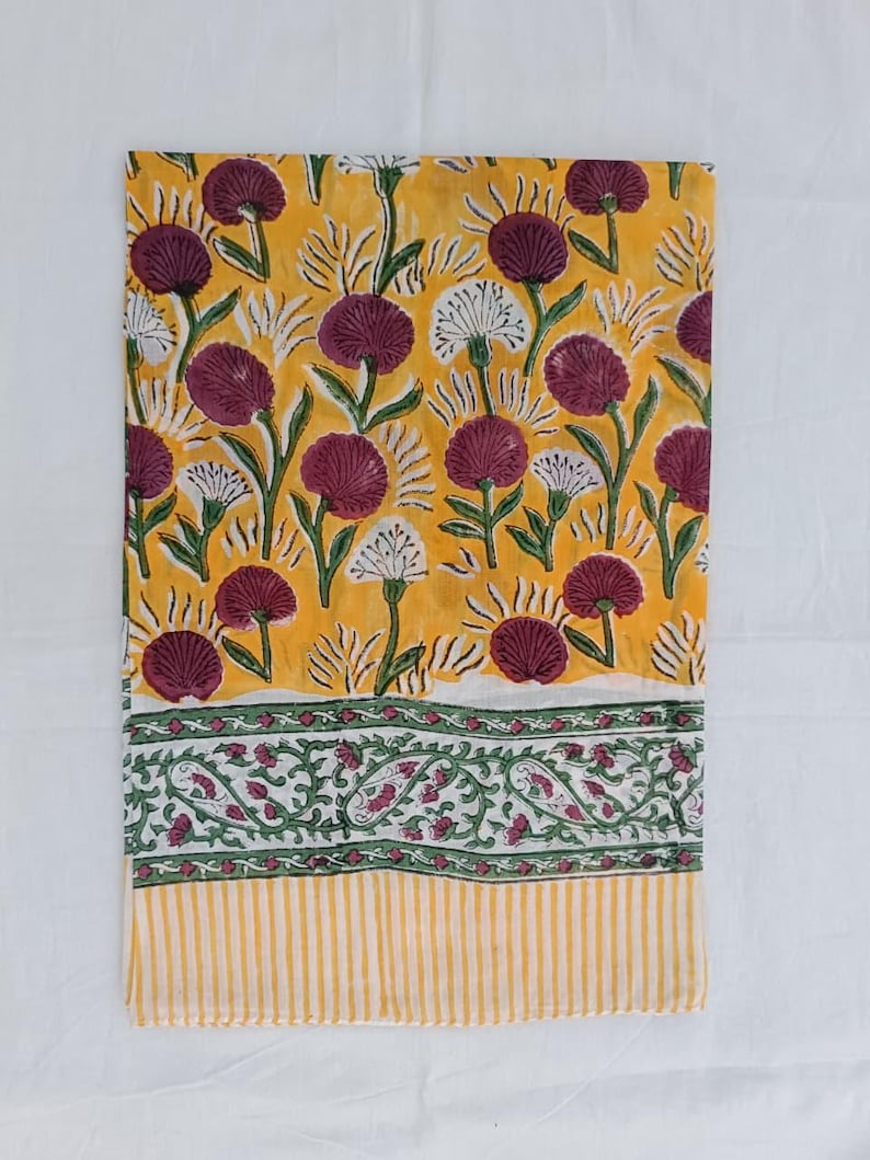 May include: A folded yellow textile with a floral pattern. The design features burgundy and white flowers with green stems and leaves. The bottom border has a green and white paisley design and yellow stripes.