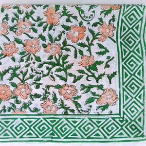 K&ouml;nnte beinhalten: Wei&szlig;er Stoff mit einem Blumenmuster aus pfirsichfarbenen Bl&uuml;ten und gr&uuml;nen Bl&auml;ttern. Ein gr&uuml;ner geometrischer Rand umrahmt die Kanten. Das florale Design ist im Blockdruckstil gehalten und erzeugt eine rustikale, handgemachte &Auml;sthetik.