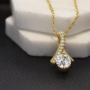May include: A gold necklace with a pendant featuring a large, clear, round gemstone surrounded by smaller, clear gemstones. The pendant is shaped like a teardrop and has a delicate, curved design.