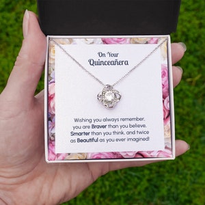 May include: A silver necklace with a crystal knot pendant in a white gift box with a message that reads "On Your Quincea&ntilde;era Wishing you always remember, you are Braver than you believe, Smarter than you think, and twice as Beautiful as you ever imagined!"