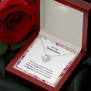 May include: A red velvet jewelry box with a silver necklace inside. The necklace has a knot pendant with a clear crystal in the center. The box has a card inside that reads "On Your Quincea&ntilde;era Wishing you always remember you are Braver than you believe. Smarter than you think, and twice as Beautiful as you ever imagined!"