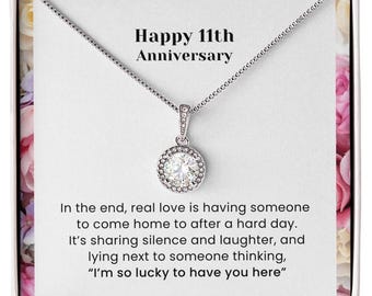 Puede incluir: Un collar de tono plateado con un colgante de piedra redonda, clara y facetada en una cadena fina. La tarjeta presenta el texto "Happy 11th Anniversary" y un mensaje sentimental sobre el amor, el silencio, la risa y la suerte de tener a alguien.