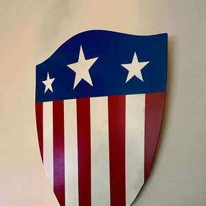 May include: A wooden shield painted with red and white stripes and blue with three white stars.