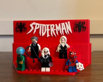 May include: A red display stand with the word "SPIDER-MAN" in white, featuring Lego minifigures of Spider-Man characters. The figures include Mysterio, a man in a suit, Black Cat, Spider-Gwen, and Spider-Man.