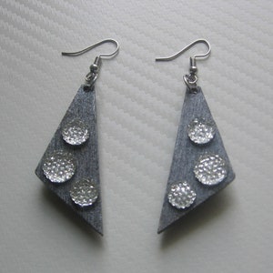 Puede incluir: Un par de pendientes triangulares plateados con tres círculos plateados con purpurina en cada pendiente.