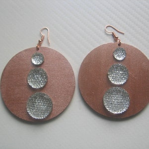 Puede incluir: Un par de pendientes de disco grandes de color cobre. Cada pendiente presenta tres adornos circulares plateados y texturizados. Los pendientes tienen ganchos para las orejas de color cobre.