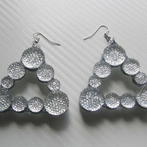 Puede incluir: Un par de pendientes de plata en forma de triángulo con un acabado brillante. Cada pendiente está formado por varios círculos pequeños.