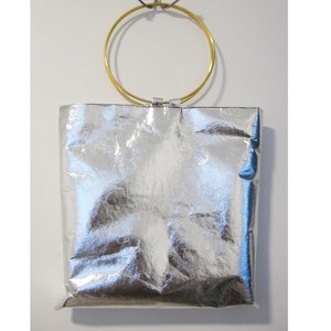 Puede incluir: Un bolso tote metálico plateado con un asa de anillo dorado.