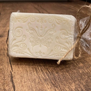 May include: A white bar of soap with a decorative butterfly design wrapped in clear plastic and tied with twine.