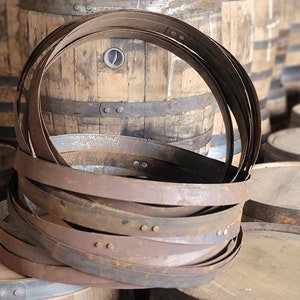 May include: A stack of rusty metal barrel hoops, likely used for making wooden barrels. The hoops are stacked on top of each other, with the top hoop being the most visible. The hoops are made of metal and have a rusty brown color. The hoops are used to hold the staves of a barrel together.