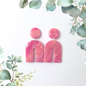 Könnte beinhalten: Ein Paar rosafarbene und weiße marmorierte bogenförmige Ohrringe mit silbernen Haken.