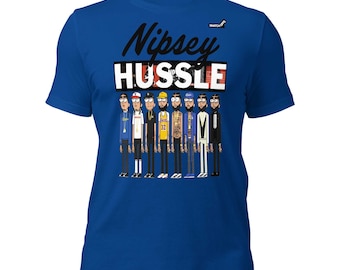 May include: A royal blue short-sleeve t-shirt featuring a graphic print of Nipsey Hussle in various outfits. The text "Nipsey HUSSLE" is printed in black and white above the illustrated figures. The design includes a small logo in the top right corner.