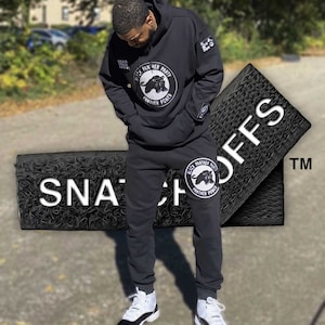 Puede incluir: Sudadera con capucha negra con un logotipo de pantera negra y el texto "Black Panther Party" y "Panther Power". La sudadera se combina con pantalones de chándal negros y zapatillas blancas y negras.