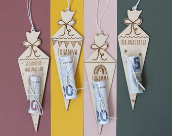 May include: Four wooden cone-shaped gift bags with money inside. The bags are decorated with a bow and a string. The bags are labeled with the names "Schulkind Maximilian", "Johanna", "Für Emma", and "Für Anastasia".