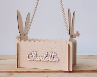 May include: A wooden Easter basket with bunny ears and a rope handle. The basket is personalized with the name "Charlotte".