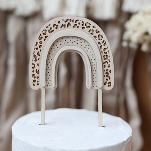 Pode incluir: Um topo de bolo de arco-íris de madeira com um design de estampa de leopardo. O topo é feito de três camadas e tem um acabamento branco. É perfeito para adicionar um toque de fantasia a qualquer bolo.