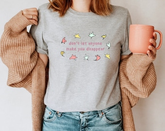 May include: A grey t-shirt with the text "don't let anyone make you disappear" in pink lettering surrounded by colourful abstract shapes.