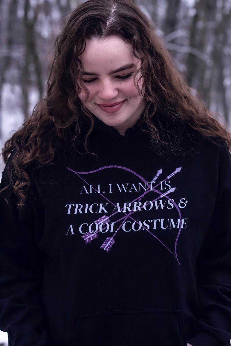 Marvel Hawkeye tv show hoodie inspired by Kate Bishop's quotes to Clint Barton, “All I Want Is Trick Arrows & A Cool Costume," with art of bow and arrows. Perfect merchandise or gift for a Marvel fan!