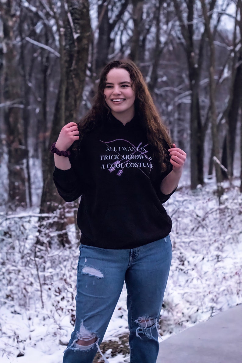 Marvel Hawkeye tv show hoodie inspired by Kate Bishop's quotes to Clint Barton, “All I Want Is Trick Arrows & A Cool Costume," with art of bow and arrows. Perfect merchandise or gift for a Marvel fan!