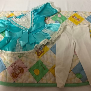 May include: A turquoise satin dress with white lace trim and a matching white satin bow. The dress is paired with white pants.