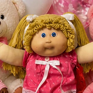 May include: A central doll with blonde yarn hair in a pink dress, surrounded by four smaller dolls in pink and purple outfits, two large plush teddy bears, heart-shaped balloons, chocolate brownies, cookies, and a bowl of pink candies.