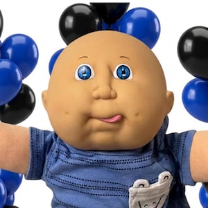 May include: A bald doll with blue eyes and a tongue sticking out, wearing a blue striped t-shirt with a small white pocket and black pants. The doll is surrounded by black and blue balloons, toy trains, a red sports car, a blue sedan, and trucks.