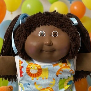 May include: A dark-skinned doll with dark brown yarn hair tied with light blue ribbons, wearing a light blue sleeveless top featuring a colorful animal print, white socks with lace trim, and white shoes, surrounded by small teddy bears and balloons.