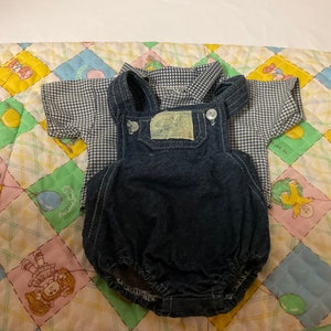 May include: A blue and white gingham shirt and denim dungarees for a baby. The dungarees have a white label with the text "Size 6 Months" on it.