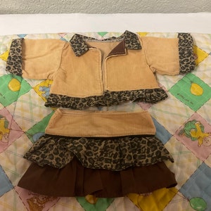 May include: A tan corduroy jacket with a leopard print trim and a matching skirt. The skirt has a brown ruffle at the bottom.