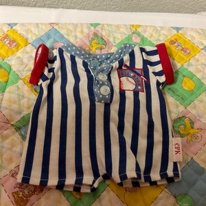 May include: A blue and white striped onesie with red trim and a baseball patch that says "All Stars". The onesie has a button closure and is labelled "CPK".