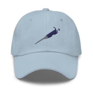May include: A light blue baseball cap with an embroidered image of a pipette, a laboratory tool used for transferring small volumes of liquid.