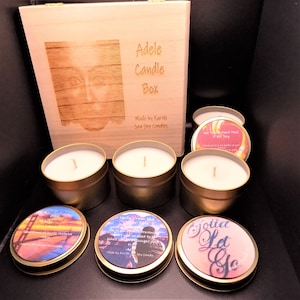 May include: A wooden box with the words "Adele Candle Box" engraved on the front. The box is open and contains six small candles with various labels, including "Out of the Blue Uninvited Candle", "Hello From the Other Side", "We Could Have Had It All Soy", and "Got to Let Go".