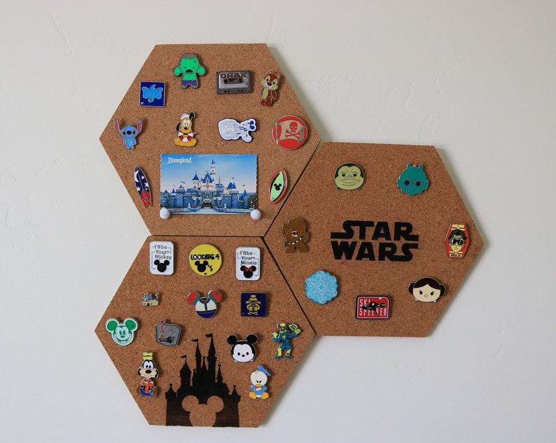 May include: A corkboard with a hexagonal shape is covered in pins. The pins are various colors and feature characters from Disney, Star Wars, and other popular franchises. The corkboard is a great way to display your favorite pins and add a touch of personality to your home.