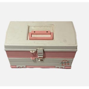 May include: A vintage, two-tone, plastic storage box in white and pink. The box has a rectangular shape with a handle and a latch closure. The box has the words "POP POP" printed on the front.