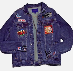 May include: A dark blue denim jacket with multiple embroidered patches. Patches include a butterfly, a rainbow fish, and the text "STAY WEIRD". The jacket has a button-up front and buttoned cuffs.