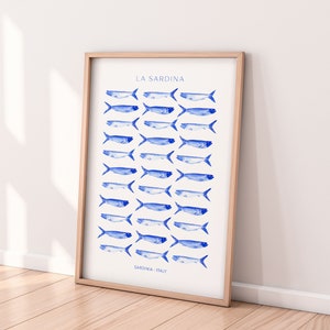 Puede incluir: Una impresi&oacute;n enmarcada con fondo blanco e ilustraciones de peces en acuarela azul. El texto "LA SARDINA" est&aacute; en la parte superior de la impresi&oacute;n y "SARDINIA, ITALY" en la parte inferior.