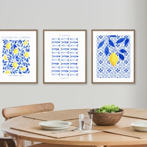Puede incluir: Tres impresiones de acuarela enmarcadas con un esquema de color azul y blanco. Las impresiones representan limones, peces y una rama de limonero. Las impresiones est&aacute;n colgadas en una pared blanca sobre una mesa de madera.
