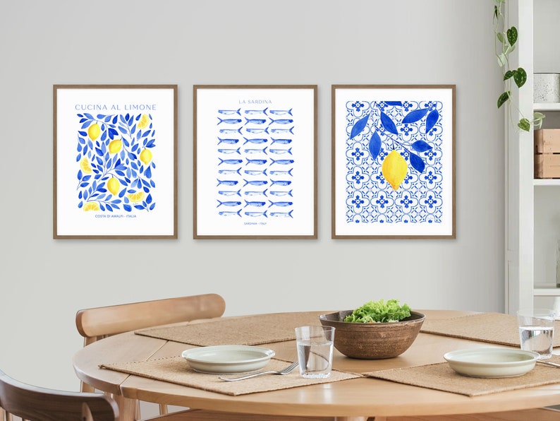 Puede incluir: Tres impresiones de acuarela enmarcadas con un esquema de color azul y blanco. Las impresiones representan limones, peces y una rama de limonero. Las impresiones est&aacute;n colgadas en una pared blanca sobre una mesa de madera.