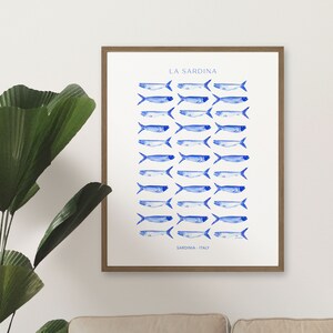 Puede incluir: Una impresi&oacute;n enmarcada con fondo blanco e ilustraciones de sardinas en acuarela azul. El texto "LA SARDINA" est&aacute; en la parte superior de la impresi&oacute;n y "SARDINIA, ITALY" en la parte inferior.