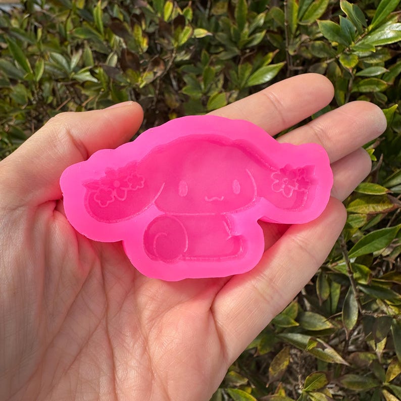 Puede incluir: Molde de silicona rosa de un perro de dibujos animados con una flor en la cabeza. El molde est&aacute; dise&ntilde;ado para hacer manualidades de resina.