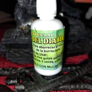 May include: A white bottle with a green label that reads "ESPECIAL DEL DIABLO" and instructions for use. The bottle is sitting on a red and black surface.