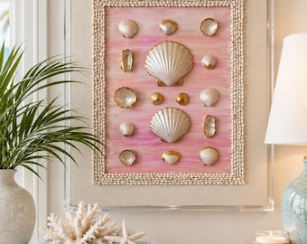 May include: A rectangular wall art piece featuring a pink watercolor background with various white and gold-toned seashells arranged in a grid. The artwork is encased in a clear acrylic frame with a border made of small, light-colored seashells.