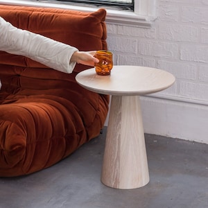 May include: A white wooden side table with a round top and a conical base. A glass of amber liquid sits on the table.